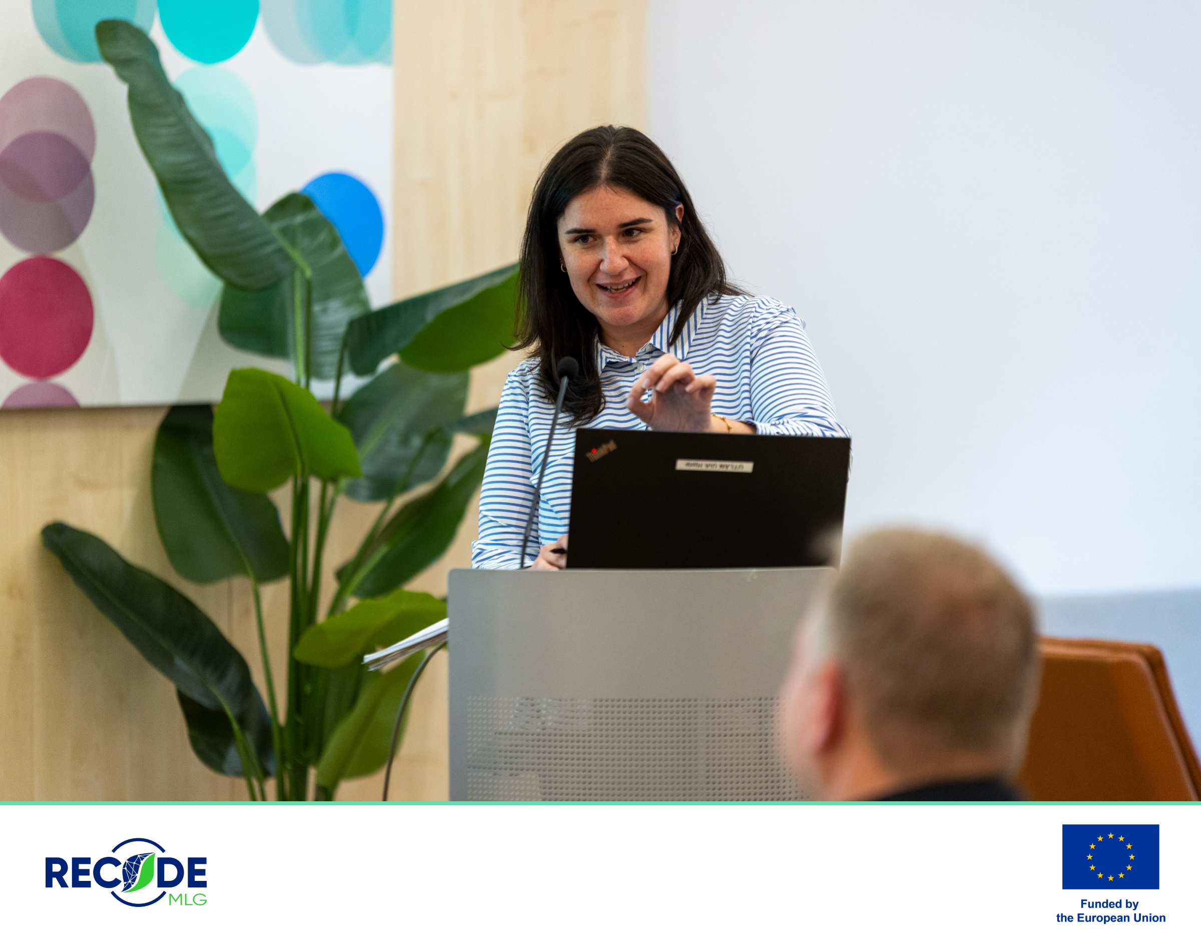 Gloria Ziglioli speaking behind a lectern with a laptop and microphone at the Brussels workshop. RECODE MLG and EU funding branding appears below the photograph.